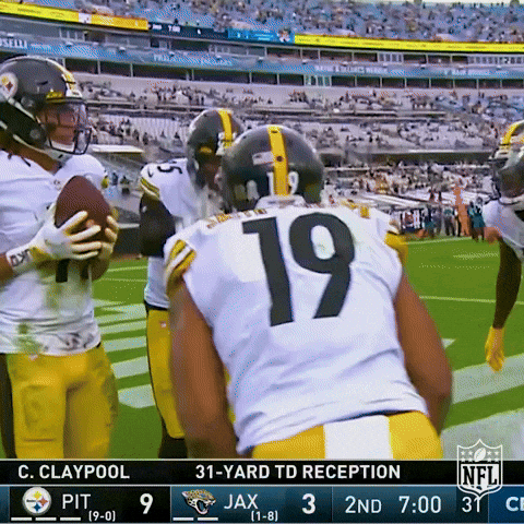 Sports gif. A bunch of players from the Pittsburgh Steelers are gathered in a circle and are singing happy birthday to Juju-Smith Schuster, waving their arms like a conductor. They hold up the football to Juju and he blows out the faux candle on the football.