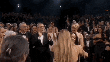 Oscars 2024 GIF. Billie Eilish and Finneas are accepting their award for best song. In the crowd, Margot Robbie gives Eilish a tight hug while they momentarily rock side to side together. 