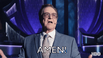 TV gif. Actor John Goodman as Dr. Eli in The Righteous Gemstones wears tinted Aviator glasses and a nice suit, with an over ear microphone next to his mouth. He raises his arms up to the heavens, looks up, and shouts, “Amen!”
