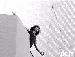 Celebrity gif. Black and white video of Criss Angel shouting to the crowd below with his arms spread wide fades into a colored video of an older woman shrugging with her hands in the air and a bewildered expression across her face.