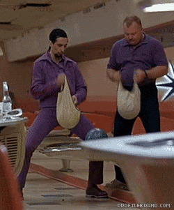 Movie gif. John Turturro as Jesus Quintana in The Big Lebowski standing by the bowling ball return with a teammate, both polishing their balls.
