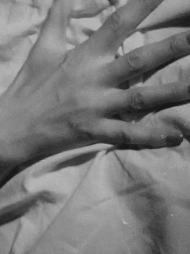 Video gif. Black and white close-up of a hand gripping onto the sheets.