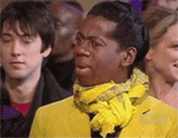 TV gif. Jay Alexander, wearing a yellow suit jacket and yellow scarf, flails his hands in confusion.
