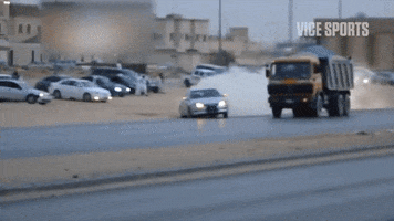 Video gif. A silver sedan speeds down a city street and begins to drift, does a full spin but gains control and continues forward.