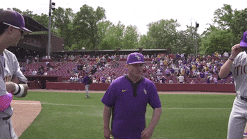 Sports gif. LSU baseball coach Jay Johnson runs towards the team and gets everyone hyped up on the field, pumping his arms excitedly.