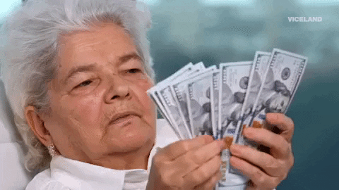 Video gif. A woman with short, gray hair fans out a stack 100 dollar bills as she counts them with a deadpan expression.