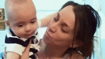 Video gif. Woman holding a baby kisses the baby's cheek, and the baby reciprocates by chomping onto her cheek.