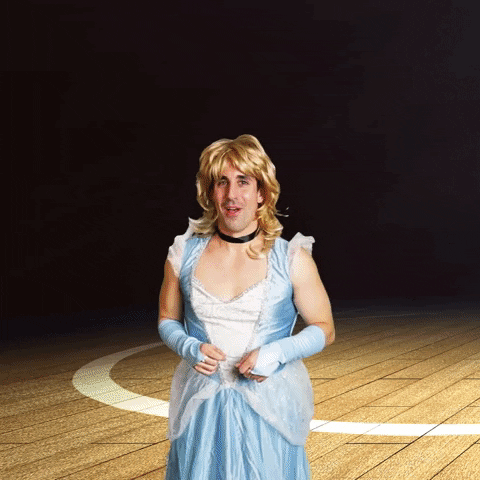 Digital compilation gif. Man in a Cinderella costume and blonde wig leans forward, holding out his hands with a big friendly smile. Colorful digital balloons float into frame as a basketball bounces across a court behind him. Text, "The fairytale continues."
