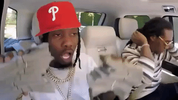 Celebrity gif. Offset and Takeoff of Migos sit in James Cordon's Carpool Karaoke car. Offset is holding two fat stacks of cash and dances with it as he shows it off. Takeoff is sitting next to him and he ties his hair back.