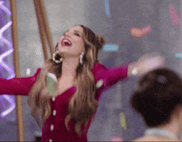 Reality TV gif. Rosanna Pansino on Baketopia dances around with her arms widespread, smiling as confetti drops from the ceiling. 