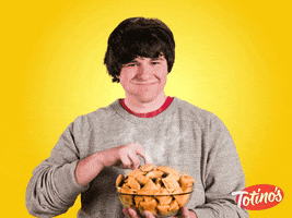 Ad gif. A man takes a pizza roll from a large bowl of steaming pizza rolls as he pops it in his mouth with a smile, nodding enthusiastically. 