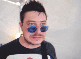 Celebrity gif. We zoom in quickly onto a member of Blink One eighty two’s face. His sunglasses are pushed down on his nose and he looks at something while grimacing in fear.