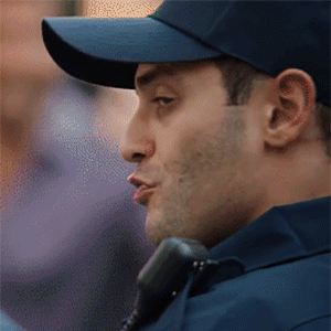 Ad gif. A handsome police officer in a blue ball cap looks over his shoulder, shrugging with a charming smirk.