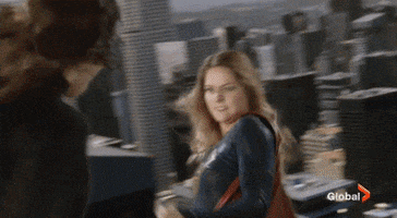 TV gif. In Supergirl, a villain shoots lasers at Melissa Benoist as Supergirl as they fight above a city. After taking a blow, Supergirl angrily punches the villain, pushing her back as we watch them floating mid-air.