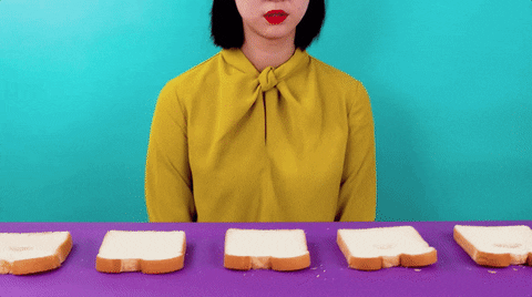 Animated gif of a woman putting her face on a slice of bread. The bread is on a table and it is moving as if on a conveyor belt.