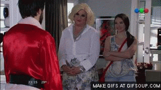 Video gif. Two women shrug at a man in a silk Santa suit as he shifts nervously.