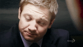 Movie gif. Jeremy Renner, in a sharp suit and tie, glances up at a person across from him before averting his eyes downward with a small disappointed shake of his head.