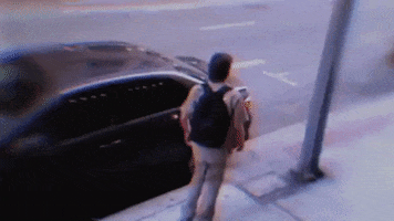 Video gif. A surveillance camera captures a man drunkenly walking down the sidewalk as he walks right into a light pole.
