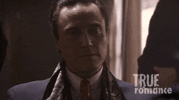 Movie gif. Christopher Walken as Vincenzo Coccotti in True Romance looks over his shoulder and then swings back around with a smug smirk on his face.