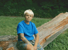 Meme gif. A person in a blonde wig and blue T-shirt sitting on a log, mimicking the Kazoo Kid meme, smiles and says, "I just wanted to say thanks, partner."