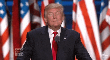 Video gif. Donald Trump stands behind a microphone in front of American flags, giving a smug smile as he shrugs and raises his arms like he doesn't have an answer. 