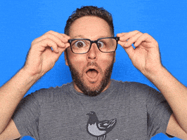 Video gif. A man holds his glasses out away from his eyes, magnifying them as if in amazement. 