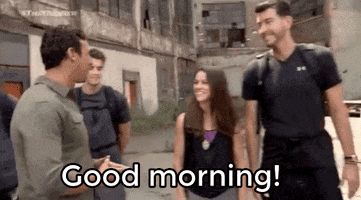 TV gif. Scene on The Runner. A Line of people with backpacks strapped on stands in front of an old, decaying building. The Host comes up to a man and woman to say, “Good morning.”