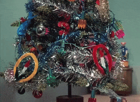 Movie gif. We gaze at a stop-motion scene of a blinking Christmas tree with presents under it, then glance over to the doorway where a young boy and girl walk in, notice the scene, and jump for joy.