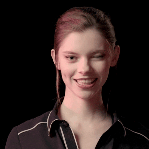 Video gif. Young woman smiles cutely and tosses us a wink.