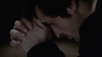 Movie gif. A close-up profile view of Jason Miller as Father Karras in The Exorcist as he prays, with his folded hands at his forehead.