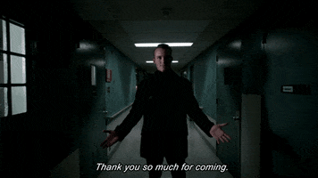 TV gif. Tom Stevens as Jason Higgins wears all black and stands in the middle of an eerily lit hallway. He holds his arms out and says, “Thank you so much for coming.”