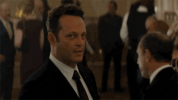 TV gif. Vince Vaughn as Frank in True Detective somberly nods and holds up a glass of champagne in a bleak cheers.