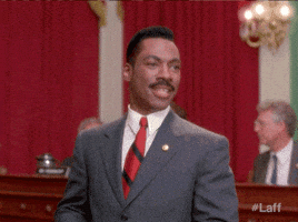Video gif. Eddie Murphy Leans back, a wide grin on his face, and emphatically claps his hands together as if to say, "There we go!"