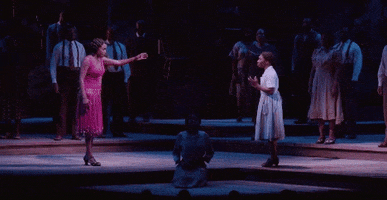 Broadway gif. Heather Headley as Shug Avery in The Color Purple walks from the left with one arm outstretched toward Cynthia Erivo as Celie walking from the right. They meet in the middle and embrace emphatically.