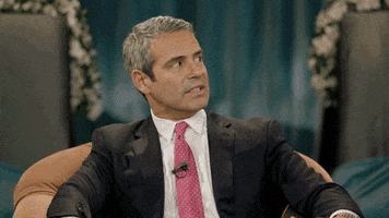 TV gif. Andy Cohen on Inside Amy Schumer sits in a character and awkwardly looks in the corner of his eye. He grits his teeth and nods, cringing at the awkward situation. 