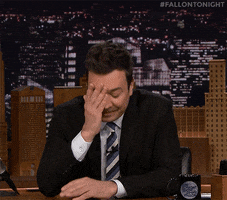 Tonight Show gif. A frustrated Jimmy Fallon sits at his desk, leaning forward with a hand over his face.