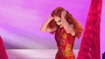 Sasha Velour performing in RuPaul’s Drag Race slowly lifts and shakes her curly red wig as hidden red rose petals cascade down her bald head, lip singing the lyrics, “I get so emotional baby,” like she’s screaming through her frustration.