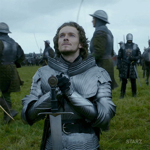 TV gif. Jacob Collins-Levy as King Henry the VII on The White Princess keels in the middle of his army getting ready for battle. His sword jabbed into the ground in front of him. He wears heavy, silver armor and looks up at the sky. He does the sign of the cross on his body and then grasps his hands together. 