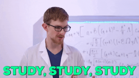 a man in a lab coat is standing in front of a whiteboard .