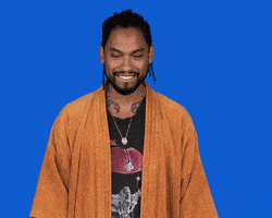 Video gif. Against a solid blue background, wearing an orange jacket, Miguel nods at us with a big smile.