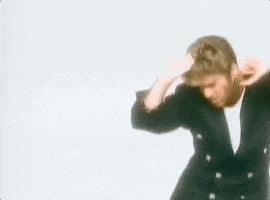Celebrity gif. In a retro music video, an excited George Michael dances happily wearing a black suit.