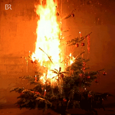 Video gif. Christmas tree is on fire and it burns to a crisp, leaving only branches behind.