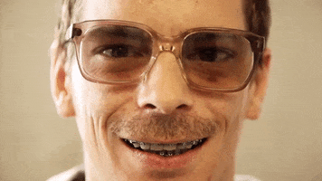Video gif. Close up of a man’s face slowly smiling at us with a brace filled mouth.