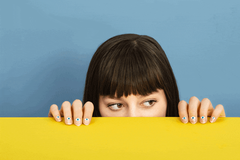 Gif of pale, brunette girl with her eyes looking around while the rest of her face is covered behind a yellow barrier.