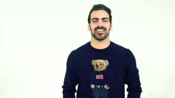 Celebrity gif. Wearing a teddy bear sweater, model Nyle DiMarco smiles says, using American Sign Language, “Happy New Year.”