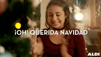Ad gif. Young woman grins and claps her hands rapidly while looking around below her. Text, "Oh! Querida Navidad."