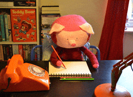 Stop motion gif. A stuffed pig is sitting at a table writing in a notebook. It looks very studious as its head tips back and forth in concentration.
