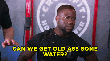 Celebrity gif. Kevin Hart stands in a Crossfit gym. He points with his thumb over to the guy next to him and he looks around as he says, “Can we get old ass some water?”
