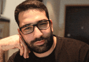 Video gif. Man with a beard, wearing glasses, rests his cheek on his fingers and gazes at us, flirting.