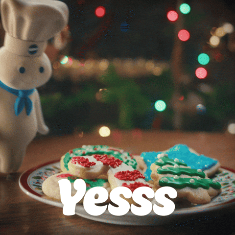 Sponsored gif. The Pillsbury Doughboy, in his iconic blue scarf and Pillsbury chef hat, gives two thumbs up to a plate of holiday cookies. Text: "Yesss"
